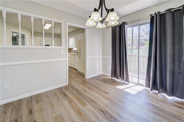 unfurnished dining area with light wood finished floors, an inviting chandelier, and baseboards