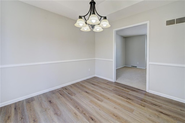 empty room with visible vents, baseboards, an inviting chandelier, and wood finished floors