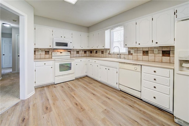 kitchen with white appliances, light countertops, backsplash, white cabinets, and a sink