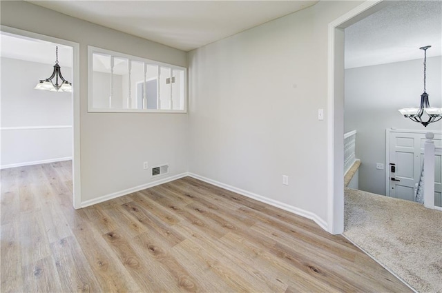 empty room with visible vents, baseboards, an inviting chandelier, and wood finished floors