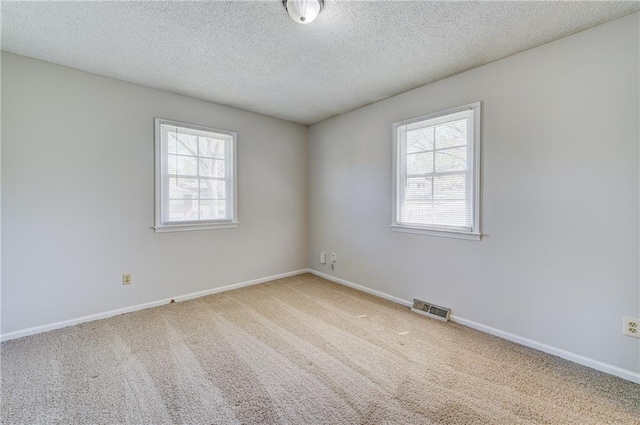 spare room with carpet, visible vents, a textured ceiling, and baseboards