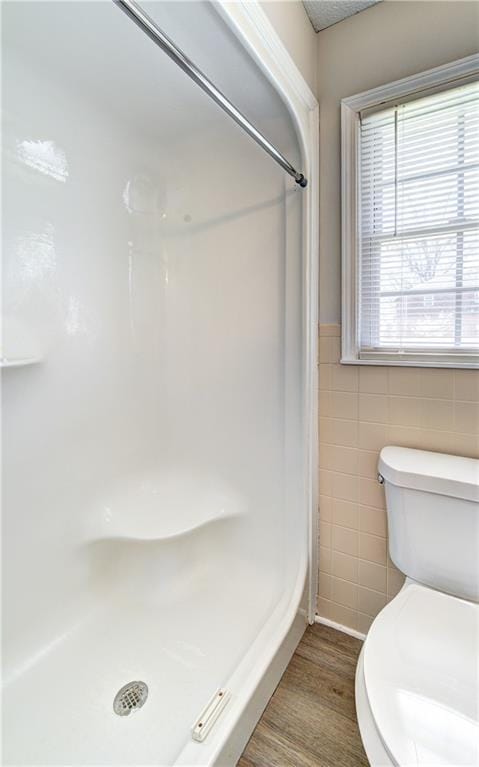 full bathroom with a wainscoted wall, tile walls, a stall shower, and wood finished floors