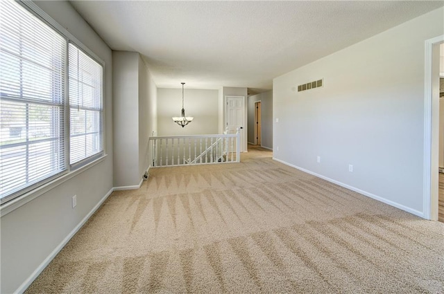 unfurnished room featuring a chandelier, baseboards, visible vents, and carpet floors