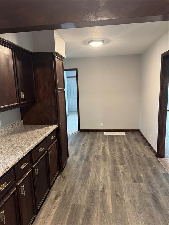 616 Prospect St, Excelsior Springs, MO 64024 - kitchen featuring dark brown cabinets, baseboards, light stone counters, and dark wood-style floors