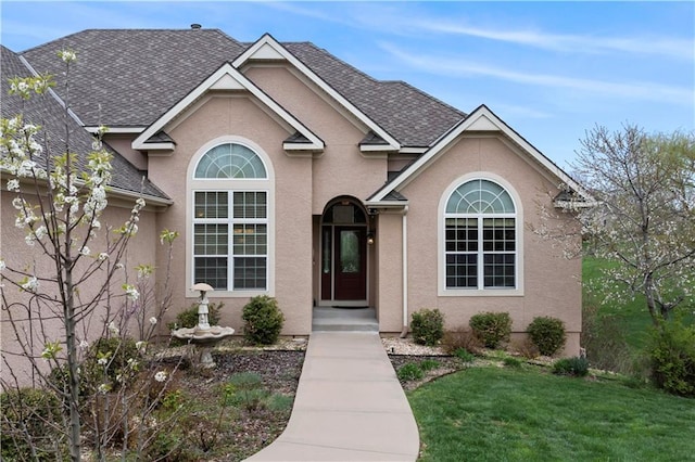 traditional-style house featuring roof with shingles, stucco siding, and a front yard