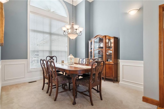 dining space with a chandelier, visible vents, light carpet, and a wainscoted wall