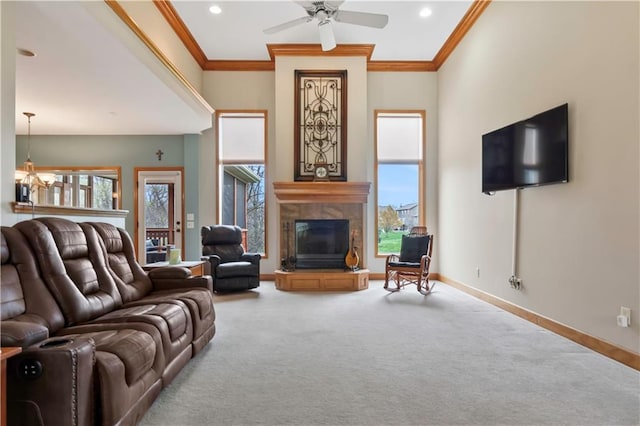 living area featuring baseboards, ornamental molding, carpet, ceiling fan with notable chandelier, and a tile fireplace