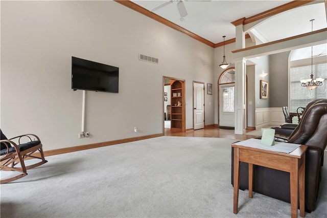 living room featuring visible vents, a high ceiling, ornamental molding, ceiling fan with notable chandelier, and carpet flooring