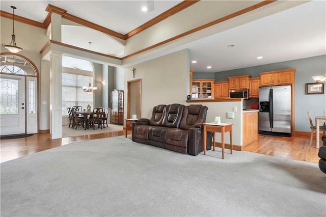 living area featuring ornamental molding, a chandelier, a high ceiling, ornate columns, and light colored carpet
