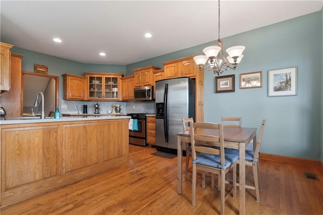 kitchen featuring tasteful backsplash, a peninsula, glass insert cabinets, stainless steel appliances, and a sink