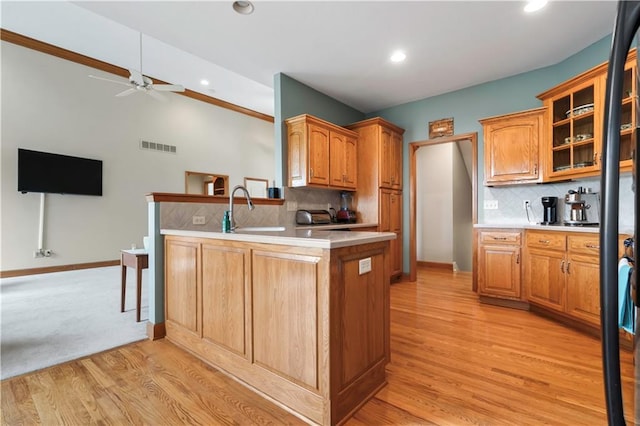 kitchen with glass insert cabinets, a sink, light countertops, a ceiling fan, and a peninsula