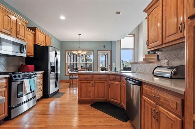 kitchen featuring brown cabinetry, appliances with stainless steel finishes, and an inviting chandelier