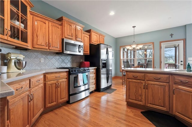 kitchen with an inviting chandelier, glass insert cabinets, brown cabinets, stainless steel appliances, and light wood finished floors