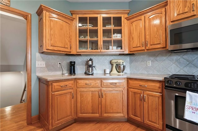 kitchen featuring stainless steel appliances, glass insert cabinets, light countertops, and brown cabinetry