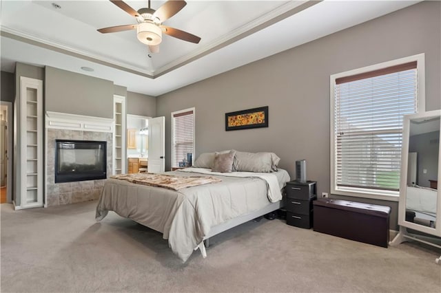 carpeted bedroom featuring a tiled fireplace, a tray ceiling, a ceiling fan, and crown molding