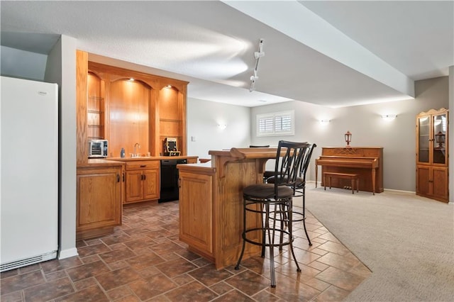 kitchen with dark colored carpet, freestanding refrigerator, black dishwasher, a kitchen bar, and stone finish flooring