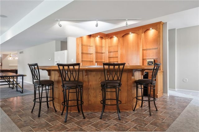 bar with stone finish flooring, indoor wet bar, baseboards, and freestanding refrigerator
