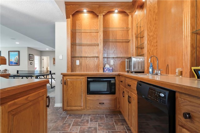 kitchen with light countertops, black appliances, brown cabinetry, stone finish flooring, and a sink