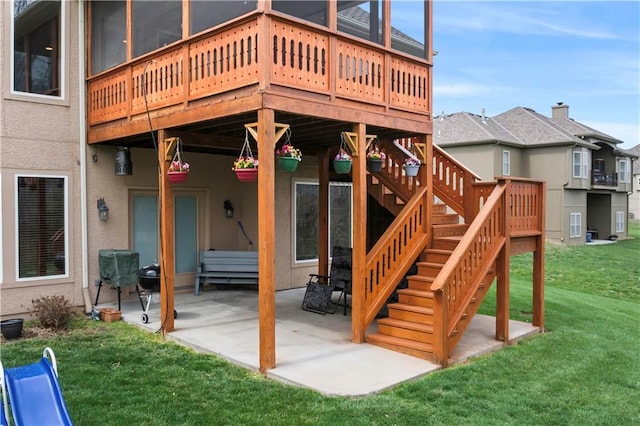 rear view of house with a wooden deck, a yard, stucco siding, a patio, and stairs