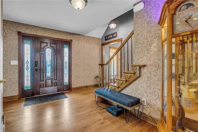 entryway with vaulted ceiling, wallpapered walls, wood finished floors, and stairs
