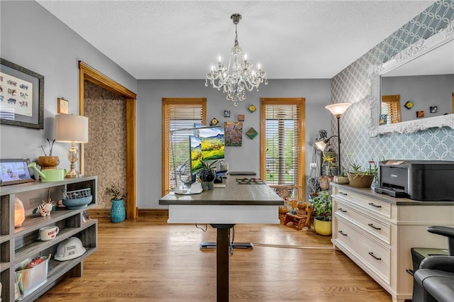 home office with wallpapered walls, an inviting chandelier, light wood-style flooring, and an accent wall