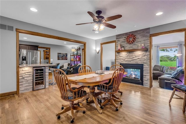 dining room featuring ceiling fan, visible vents, a fireplace, beverage cooler, and light wood-style floors