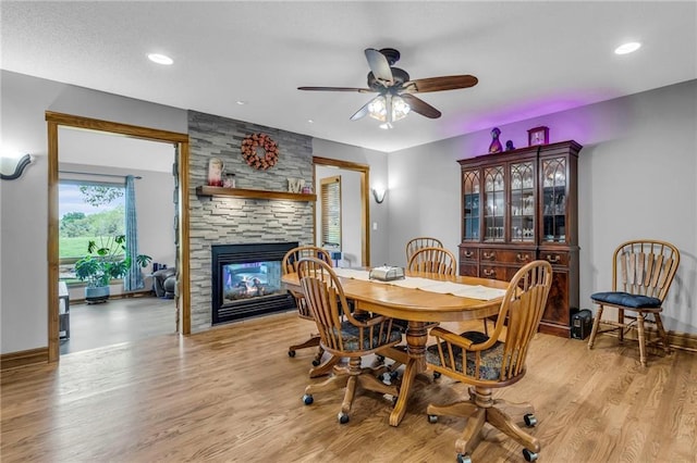 dining space featuring ceiling fan, a stone fireplace, light wood-type flooring, baseboards, and recessed lighting