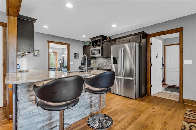 kitchen with appliances with stainless steel finishes, light stone counters, light wood-style floors, a peninsula, and tasteful backsplash