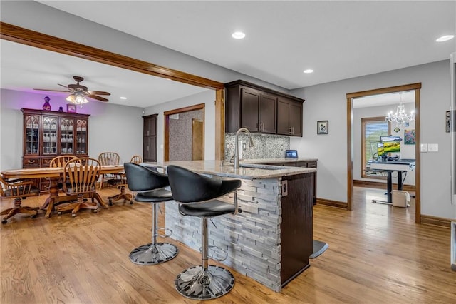 kitchen featuring dark brown cabinets, a breakfast bar, light stone counters, a sink, and light wood-style flooring