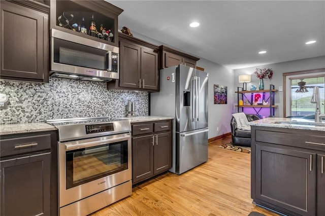 kitchen with decorative backsplash, dark brown cabinets, light wood-type flooring, a sink, and appliances with stainless steel finishes