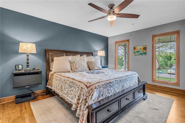 bedroom with baseboards, a wall mounted air conditioner, wood finished floors, and multiple windows