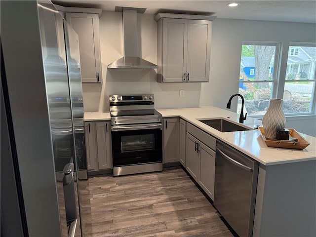 kitchen featuring wall chimney range hood, gray cabinetry, stainless steel appliances, and a sink