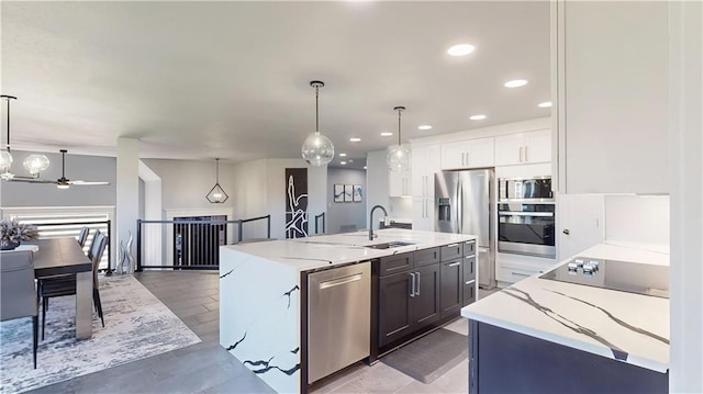 kitchen with a sink, appliances with stainless steel finishes, a kitchen island with sink, white cabinetry, and light stone countertops