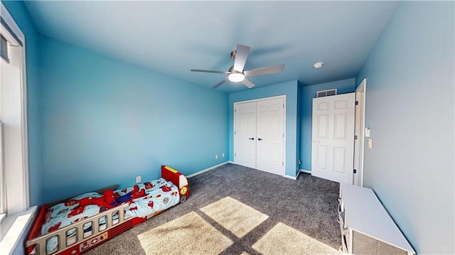 unfurnished bedroom with visible vents, a closet, baseboards, dark colored carpet, and a ceiling fan