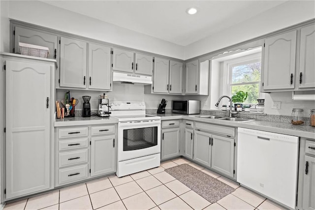 kitchen with white appliances, gray cabinets, under cabinet range hood, a sink, and light tile patterned floors