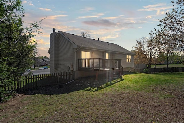 back of property featuring a lawn, a deck, fence, and a chimney
