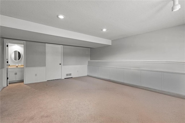finished basement with a sink, a textured ceiling, a wainscoted wall, recessed lighting, and visible vents