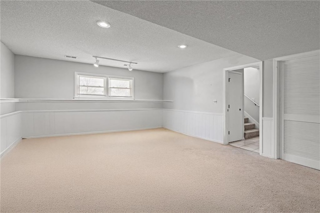 basement with carpet floors, a textured ceiling, wainscoting, and stairway