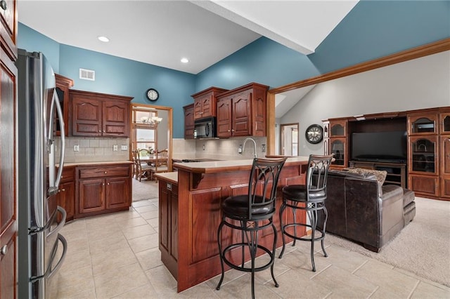 16011 Cedar St, Basehor, KS 66007 - kitchen featuring freestanding refrigerator, black microwave, a peninsula, a breakfast bar area, and tasteful backsplash