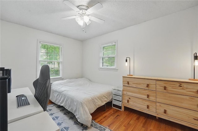 bedroom with a textured ceiling, dark wood-style flooring, ceiling fan, and multiple windows