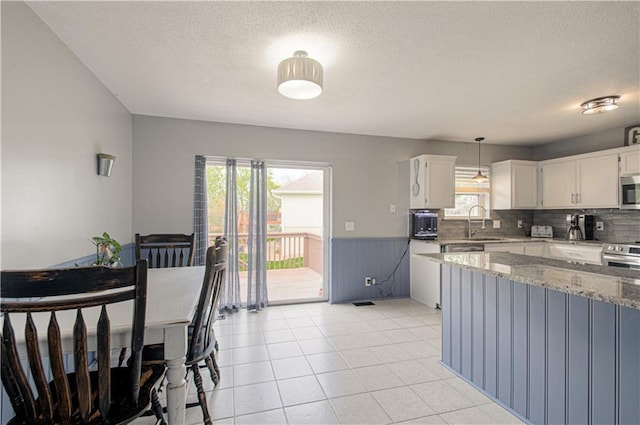 310 E 22nd St, Kearney, MO 64060 - kitchen featuring wainscoting, stainless steel appliances, a textured ceiling, and light stone countertops