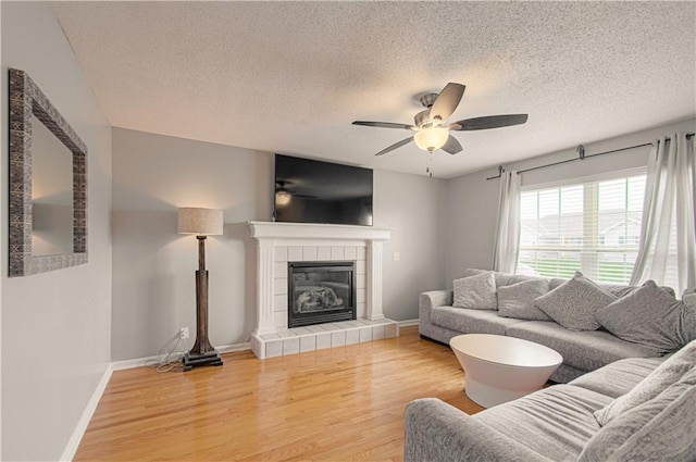 310 E 22nd St, Kearney, MO 64060 - living room with light wood-style flooring, a textured ceiling, a tiled fireplace, baseboards, and a ceiling fan