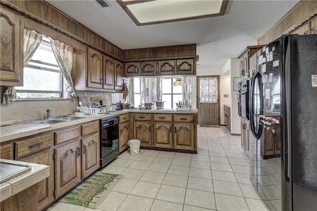 2301 S Stilwell St, Pittsburg, KS 66762 - kitchen with light tile patterned floors, a peninsula, a textured ceiling, black appliances, and a sink