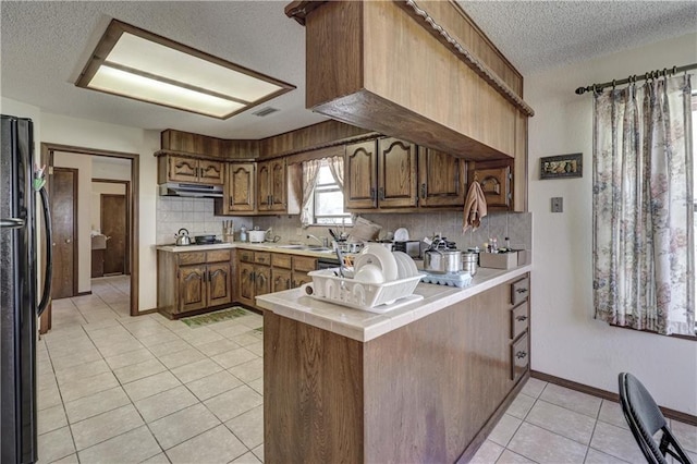 2301 S Stilwell St, Pittsburg, KS 66762 - kitchen featuring freestanding refrigerator, light tile patterned floors, a textured ceiling, under cabinet range hood, and backsplash