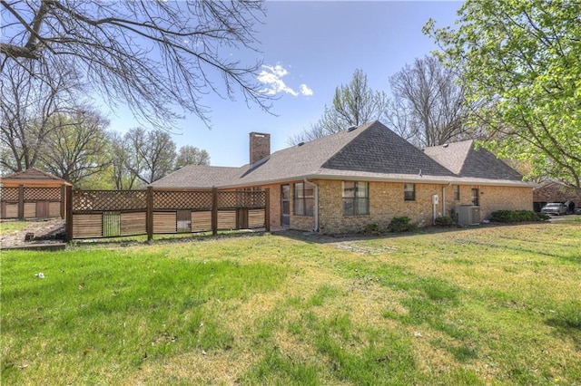 2301 S Stilwell St, Pittsburg, KS 66762 - back of property featuring roof with shingles, a chimney, brick siding, central AC unit, and a lawn