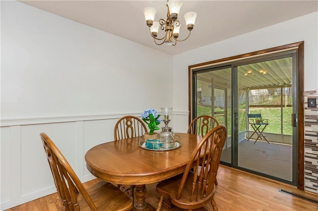 dining space featuring light wood-style floors, a decorative wall, a wainscoted wall, and an inviting chandelier