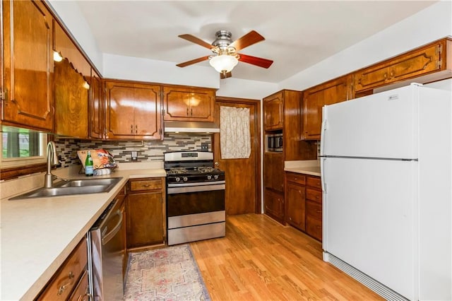 kitchen with a ceiling fan, a sink, decorative backsplash, light wood-style flooring, and appliances with stainless steel finishes