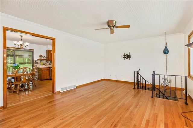 spare room with visible vents, ornamental molding, light wood-type flooring, baseboards, and ceiling fan with notable chandelier