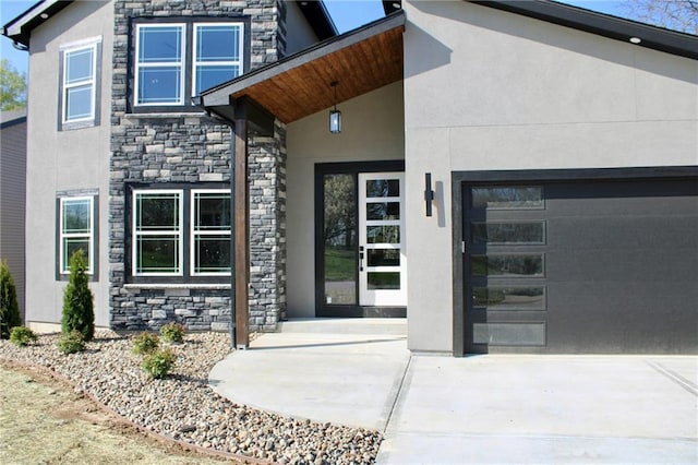 entrance to property with concrete driveway, an attached garage, stone siding, and stucco siding
