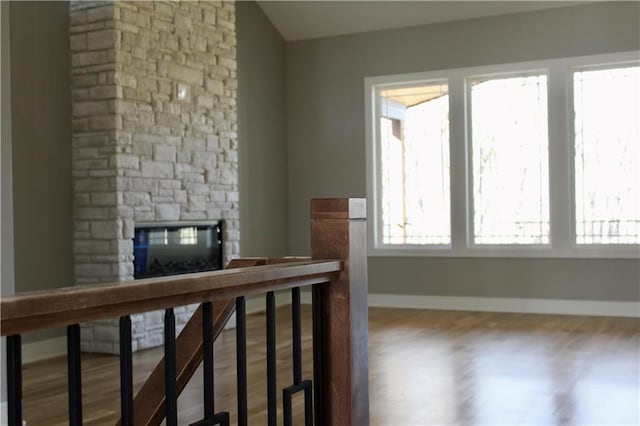 unfurnished living room featuring a stone fireplace, baseboards, and wood finished floors